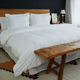 Cama con funda edredón blanco y bastones grises, banco madera-blanco