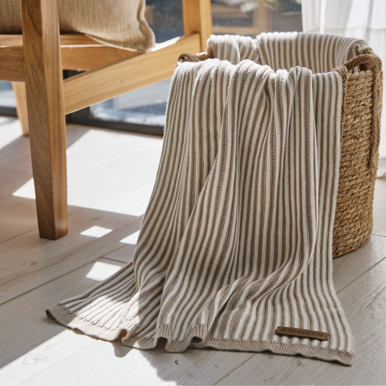 Manta beige de rayas verticales sobre piso de madera junto a canasta-beige