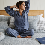 
                    
                      Mujer en pijama azul sentada en cama gris relajada-
                    
                  
