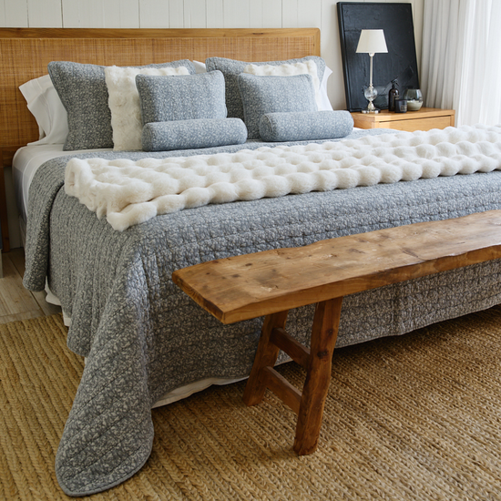 Cubrecama Leicester gris sobre cama con almohadas decorativas y banco de madera-gris