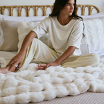 
                    
                      Mujer sentada en cama con cubrecama blanco acolchado Berna-
                    
                  