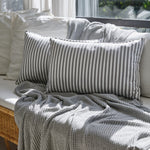 
                    
                      Almohada gris a rayas junto a mantas texturizadas en cama luminosa-gris
                    
                  