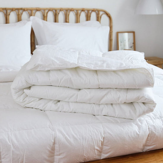 Edredón blanco antibacterial doblado sobre cama con cabecero de ratán-blanco