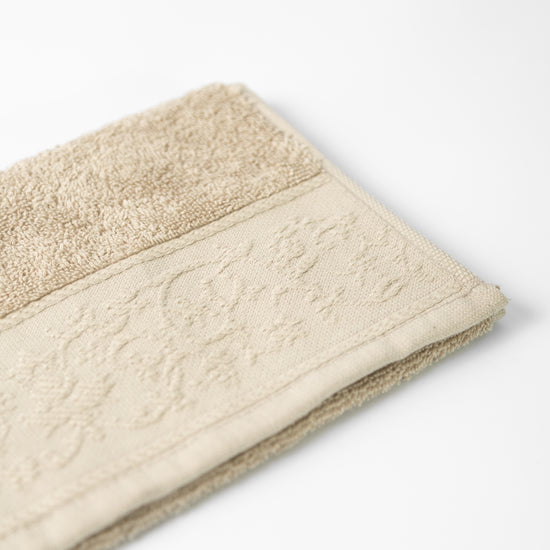 Toalla beige de algodón con textura de felpa y orilla decorativa-