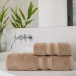 
                    
                      Set de toallas beige enrolladas con banda decorativa en baño moderno-
                    
                  