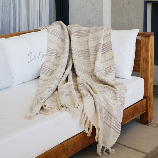 Manta Murano beige con rayas texturizadas sobre cama de madera-beige