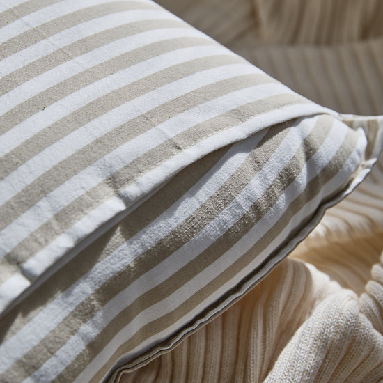 Almohada decorativa a rayas beige y blanco sobre sofá-beige