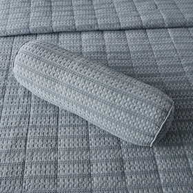 Almohada cilíndrica gris sobre colcha acolchada de textura cuadriculada-gris