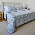 
                    
                      Cubrecama azul acolchado en cama con almohadas y cabecero gris-azul
                    
                  