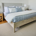 
                    
                      Cama con cubrecama azul, almohadas decorativas y cabecero tapizado gris-azul
                    
                  