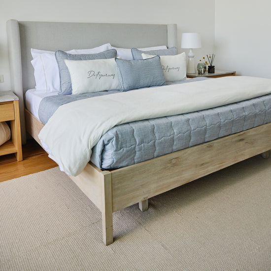 Cama con cubrecama azul, almohadas decorativas y cabecero tapizado gris-azul