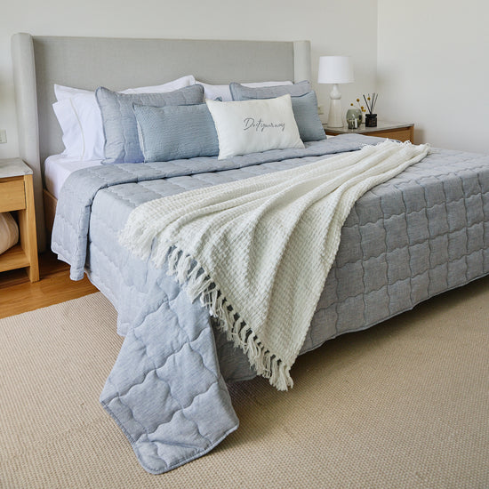 Cama con cubrecama azul, almohadas decorativas y manta de franjas blancas-azul