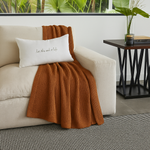 
                    
                      Manta ginger marrón sobre sofá crema con cojín blanco decorativo-
                    
                  