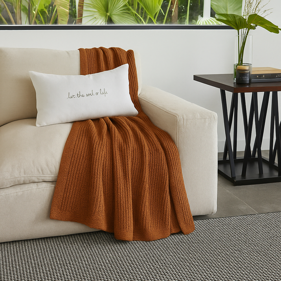 Manta ginger marrón sobre sofá crema con cojín blanco decorativo-