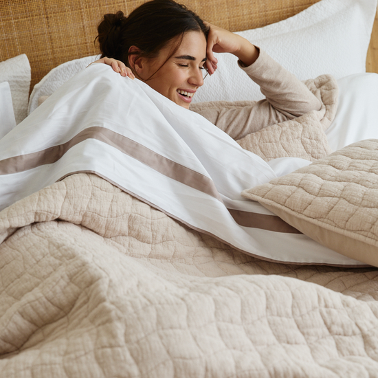 Mujer sonriente envuelta en sábanas blancas de algodón egipcio en cama-