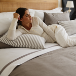 
                    
                      Mujer reclinada en cama con sábanas de algodón egipcio rayadas-
                    
                  
