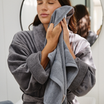 
                    
                      Mujer secando su rostro con toalla gris frente al espejo-
                    
                  
