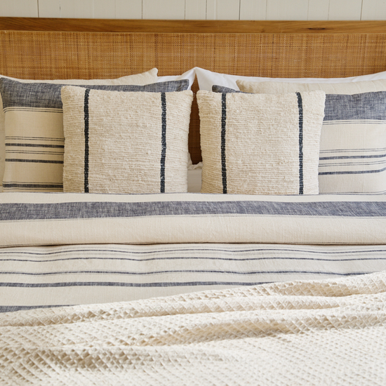 Cama con edredón azul, almohadas decorativas a rayas y cabecero de ratán-azul