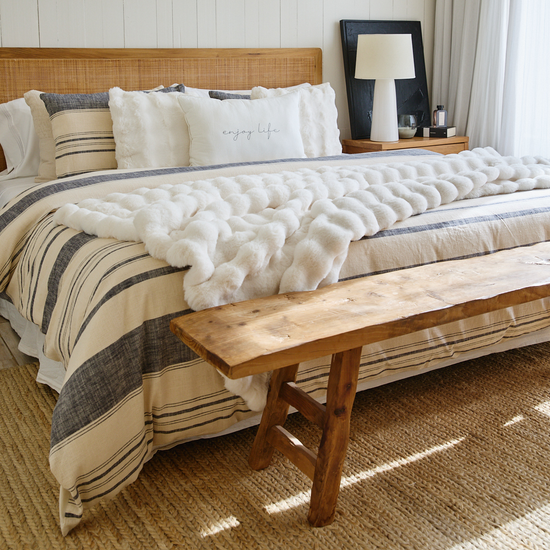 Cama elegante con edredón azul, almohadas decorativas y banco de madera-azul