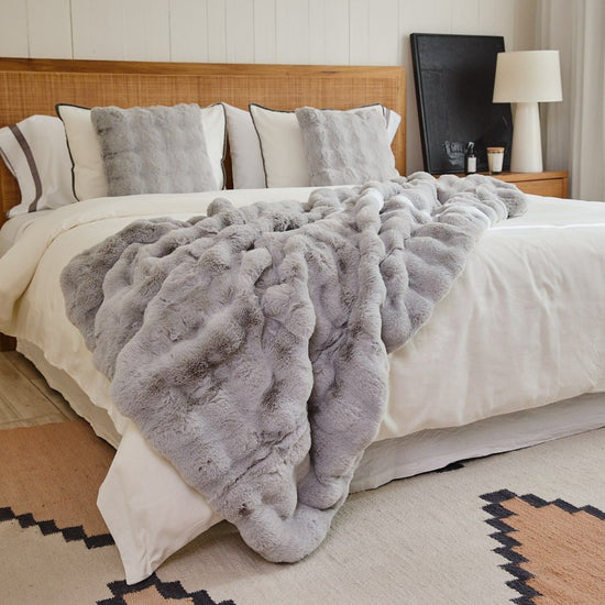 Cama con manta de piel simulada gris y almohadas decorativas-