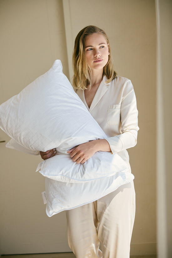 Mujer sosteniendo almohadas blancas de hotel en pijama crema-