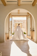 
                    
                      Novia con vestido blanco atravesando arco hacia patio de piedra-
                    
                  