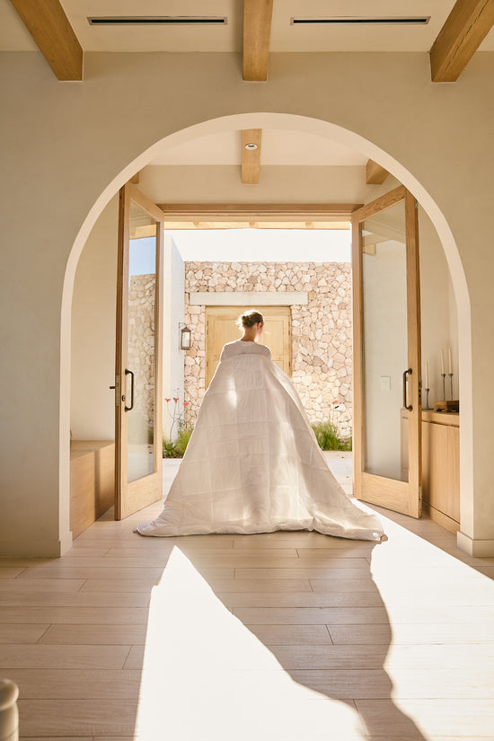 Novia con vestido blanco atravesando arco hacia patio de piedra-