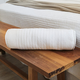 Almohada cilíndrica blanca acolchada sobre mesita de madera-blanco