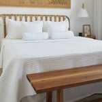 
                    
                      Cubrecama blanco Lugano sobre cama con cabecero de bambú y almohadas-blanco
                    
                  
