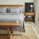 
                    
                      Dormitorio con cama de madera, sábanas grises y mesita de noche-gris
                    
                  