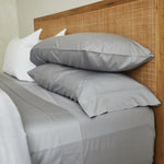 
                    
                      Cama con sábanas gris claro y almohadas grises sobre headboard de rafia-gris
                    
                  