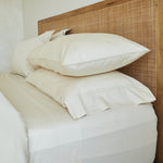 
                    
                      Cama con sábanas blancas y almohadas sobre cabecero de ratán-natural
                    
                  