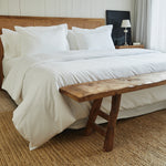 
                    
                      Cama con funda de edredón blanco y banco de madera al pie-blanco
                    
                  