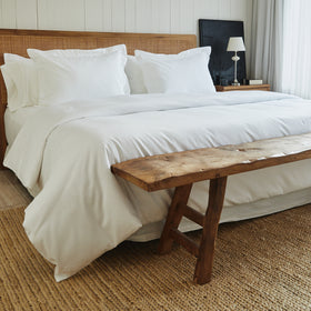 Cama con funda de edredón blanco y banco de madera al pie-blanco