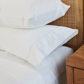 Dos fundas de almohada blancas con acabado vainilla sobre cama de madera-blanco