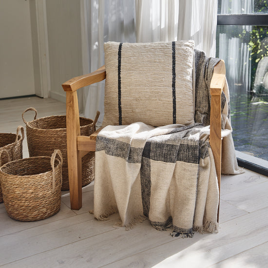 Sillón de madera con almohada y manta a rayas junto a cestas-azul