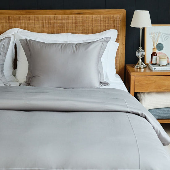Cama con funda edredón gris, almohadas blancas y mesita de noche de madera-