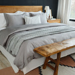 
                    
                      Cama con funda de edredón gris y festón decorativo en tonos neutros-
                    
                  