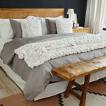 
                    
                      Cama con edredón gris, cojines blancos y banco de madera-
                    
                  