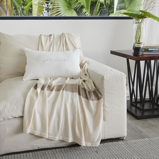 Manta Eugenia Rayas beige sobre sofá blanco junto a mesa-
