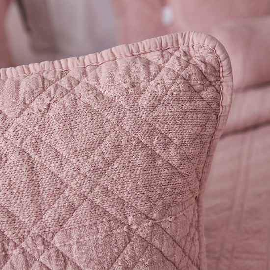 funda de almohadón cuadrado sobre cama en trama manchester-rosa
