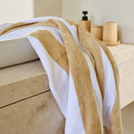 
                    
                      Toalla de playa con rayas beige y blancas sobre superficie de madera-beige
                    
                  