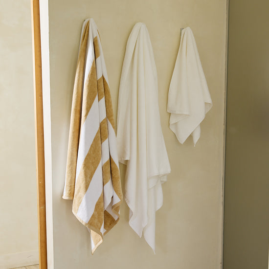 Toalla playa con rayas beige y blancas colgada en pared beige-beige