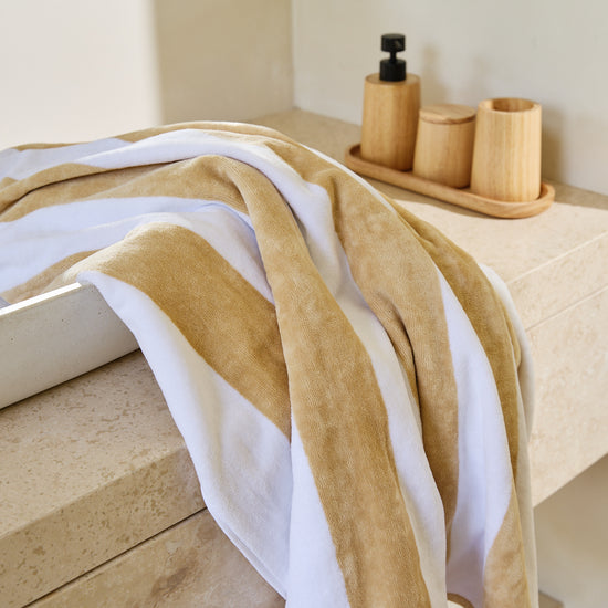 Toalla de playa con rayas beige y blancas colgada en bañera-beige