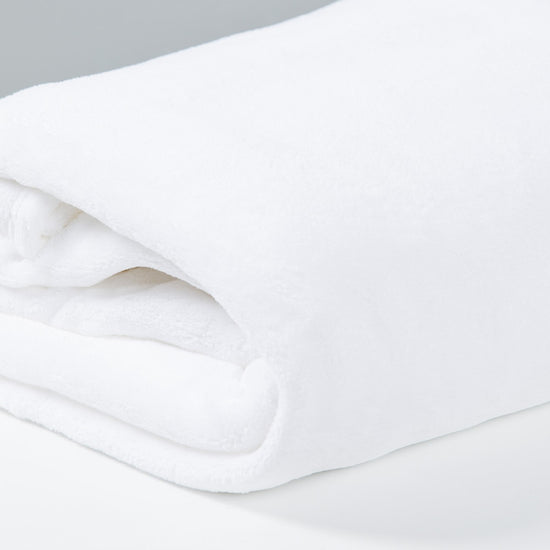 Frazada polar blanca enrollada sobre superficie gris clara-