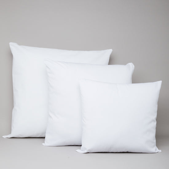 Tres cojines blancos de diferentes tamaños sobre fondo gris-blanco