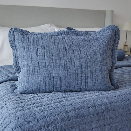 Funda de almohada azul texturizada sobre cama con cabecero gris-