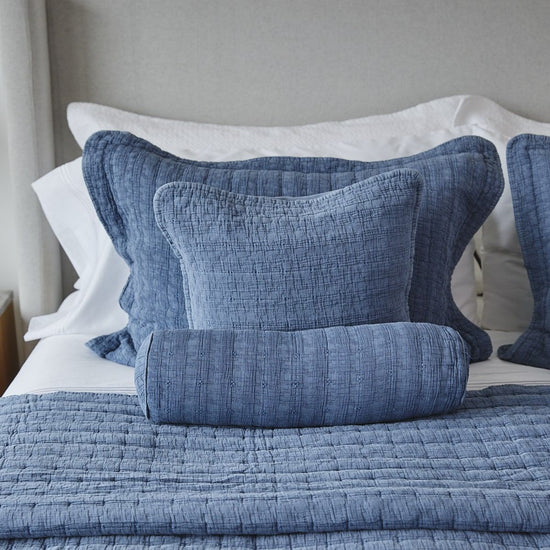Almohadas azules con volantes blancos sobre cama con colcha gris-