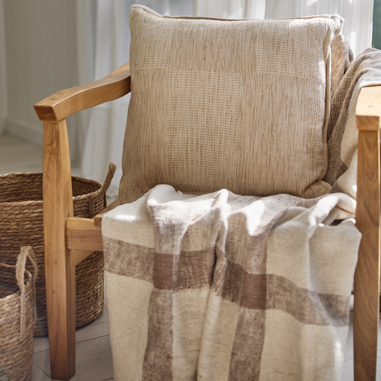Almohada beige texturizada en silla madera con manta a cuadros-beige