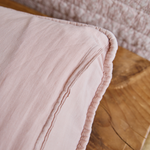 
                    
                      Detalle de funda de almohada rosa con ribete decorativo y textura-
                    
                  